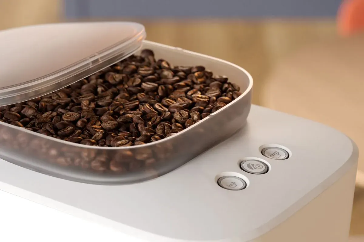 Nahaufnahme der Philips Baristina mit geöffnetem Bohnenbehälter, gefüllt mit Kaffeebohnen, darunter drei Bedienknöpfe auf der Oberseite der Maschine.