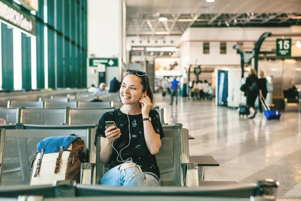 Eine Frau sitzt in einem Flughafen-Wartebereich und telefoniert mit Kopfhoerern