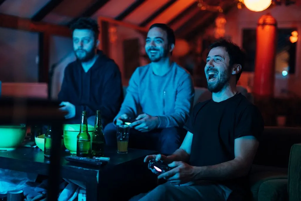 Drei Maenner sitzen zusammen auf dem Sofa und spielen Videospiele