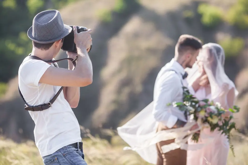 Fotograf mit Hut macht ein Hochzeitsfoto von einem Brautpaar im Freien