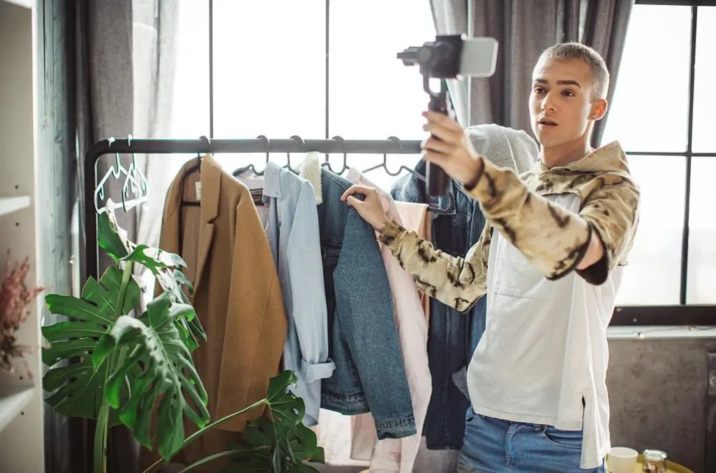Eine Person filmt sich und Kleidung an einer Kleiderstange mit einem Smartphone.