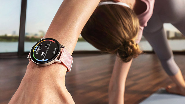 Eine Frau in Sportkleidung macht Yoga, mit einer Smartwatch am Handgelenk, die Trainingsdaten anzeigt.