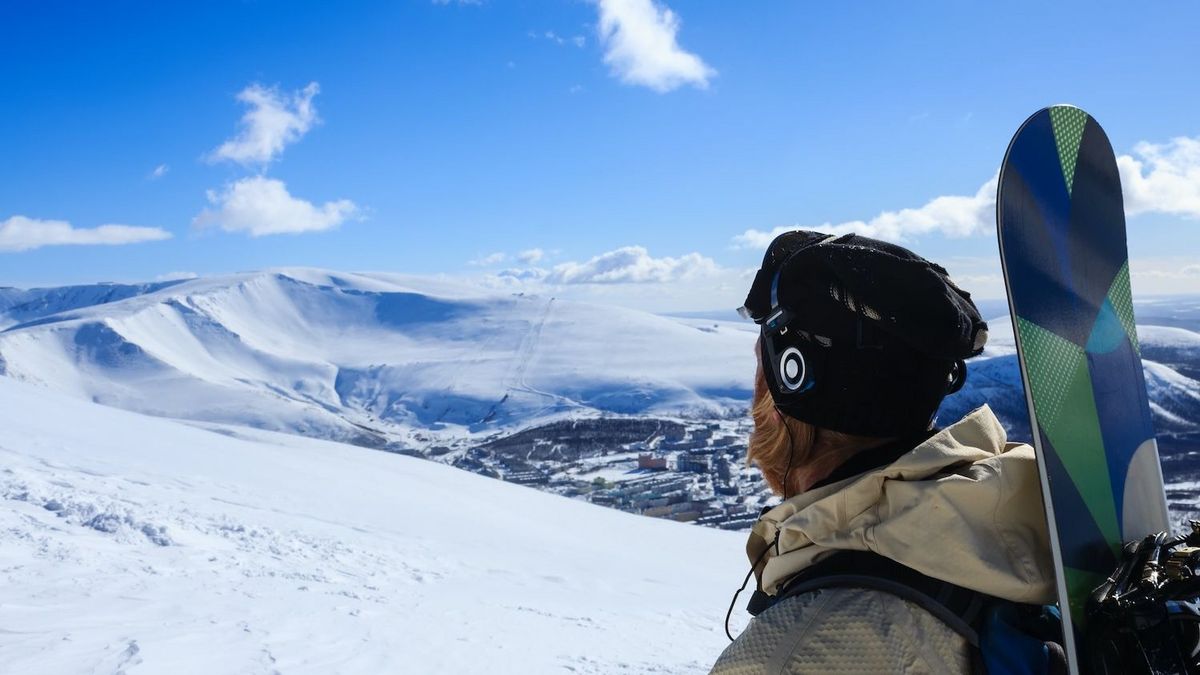 Skifahrer mit Kopfhoerern blickt auf verschneite Berglandschaft