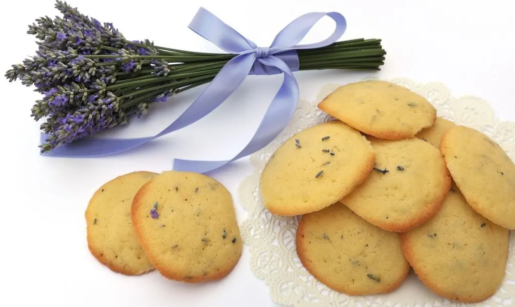 Helle Kekse mit Lavendel neben einem Lavendelstrauß mit Schleife auf weißem Hintergrund.
