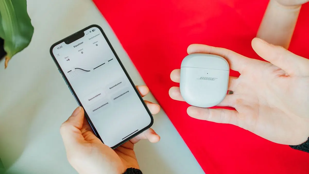 Eine Hand hält ein Smartphone mit Equalizer-App, die andere Hand hält ein weißes Bose Ladecase.