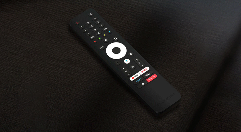 Eine schwarze TV-Fernbedienung liegt auf einer dunklen Oberfläche. Die Fernbedienung hat Tasten für Zahlen, Navigation und Streaming-Dienste.