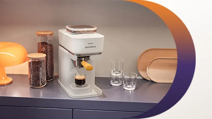 Philips Baristina Kaffeemaschine auf einer Küchenarbeitsplatte, daneben Kaffeebohnenbehälter, Gläser und Deko, im Siebträger steht ein frisch gebrühter Espresso.