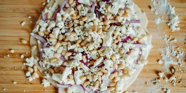 Ungebackener Flammkuchen mit Zwiebel, Feta und Pinienkernen.