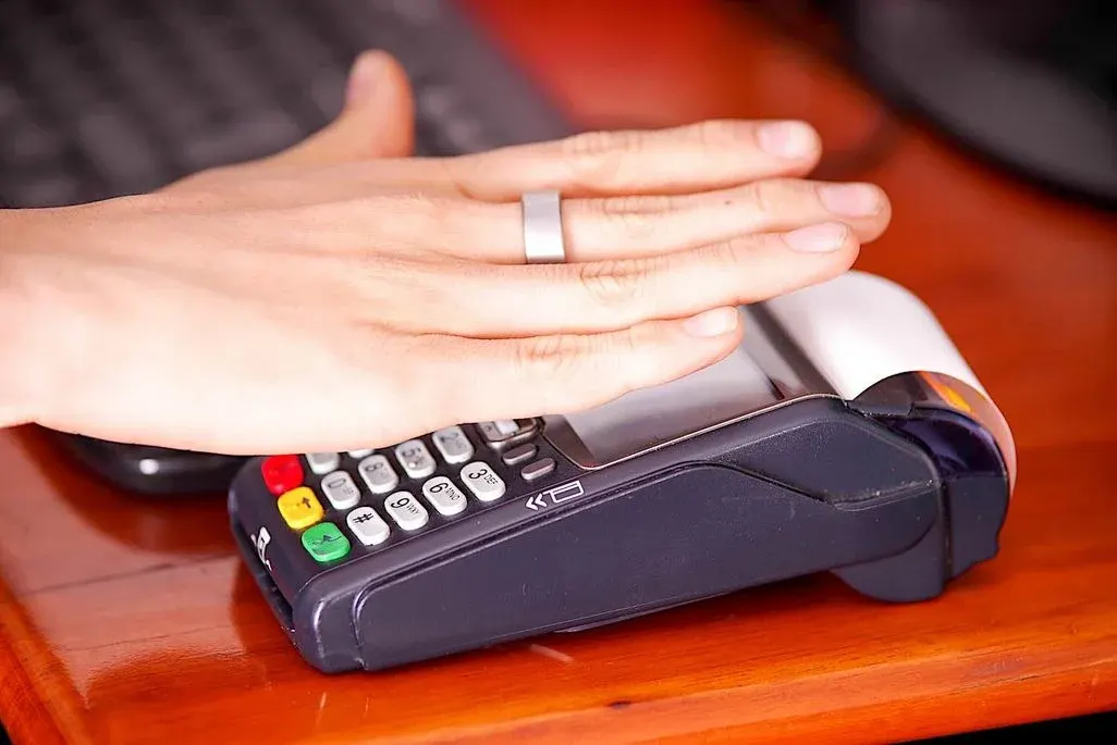 Hand mit einem silbernen Smart‑Ring hält über ein Kartenlesegerät zur kontaktlosen Zahlung. 
