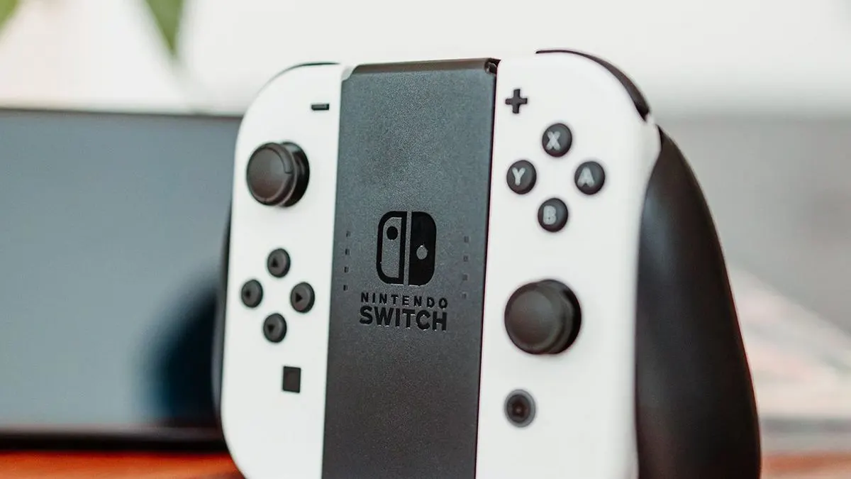Nintendo Switch Controller mit weissen Joy-Cons steht vor einer unscharfen Konsole.