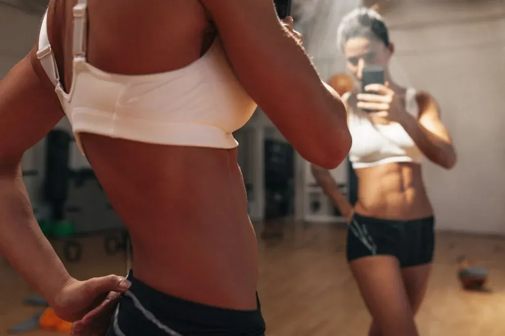 Sportliche Frau macht ein Selfie vor dem Spiegel von ihrem Sixpack.