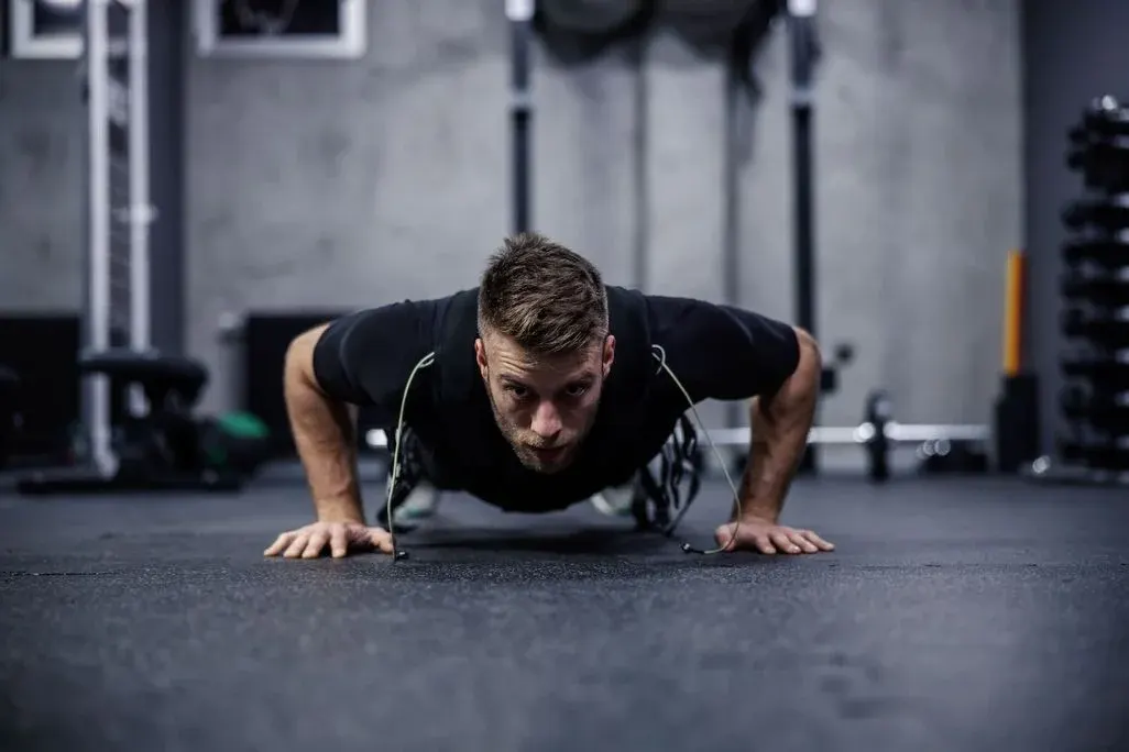  Mann im Fitnessstudio macht Liegestütze in Bodennähe und trägt dabei einen EMS‑Anzug mit sichtbaren Kabeln.