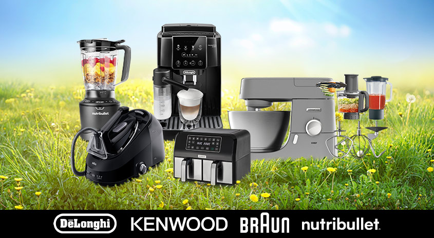 Auf einer Wiese stehen Küchengeräte wie Mixer, Kaffeemaschine und Fritteuse. Im Hintergrund ist ein blauer Himmel zu sehen.