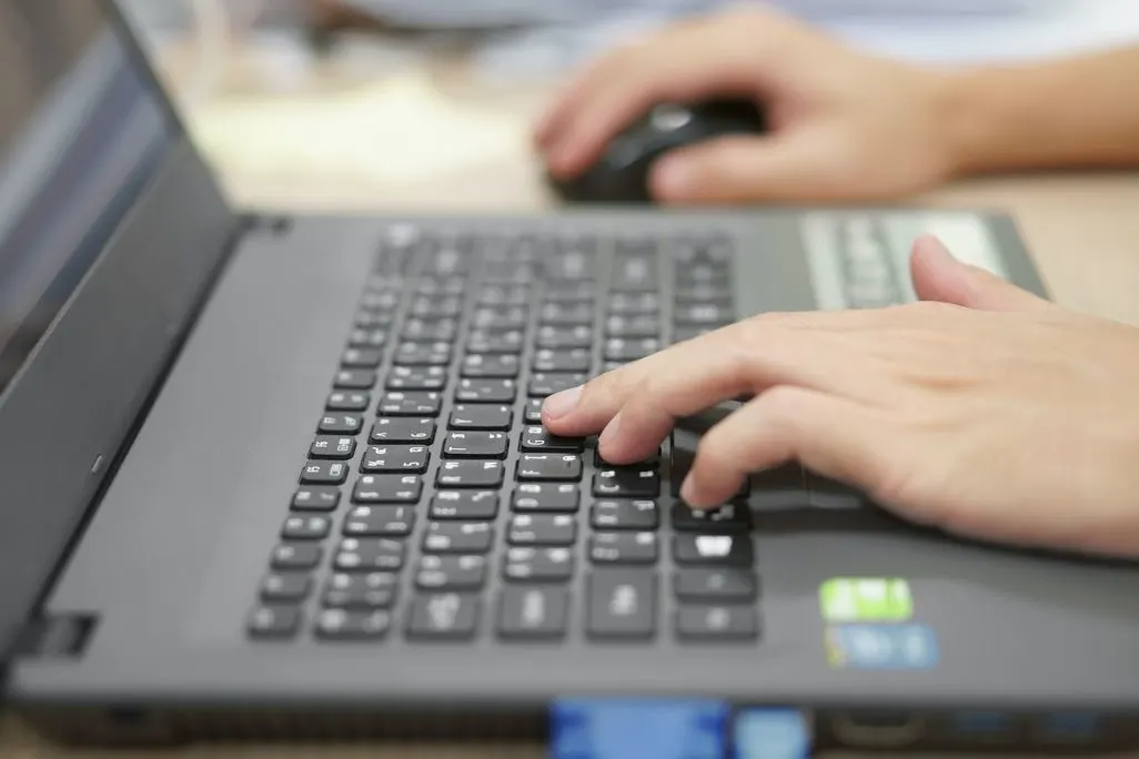 Hände tippen auf schwarzer Laptop-Tastatur mit Computer-Maus daneben.