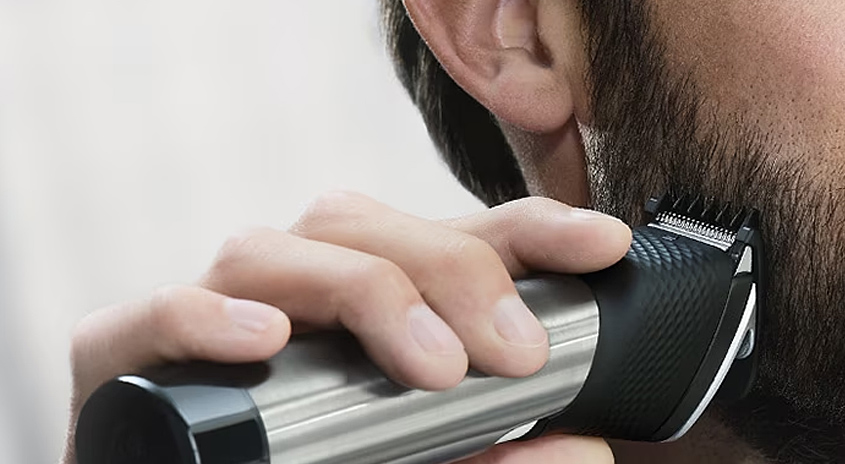 Ein Mann trimmt seinen Bart mit einem silbernen und schwarzen Bartschneider vor einem weißen Hintergrund.