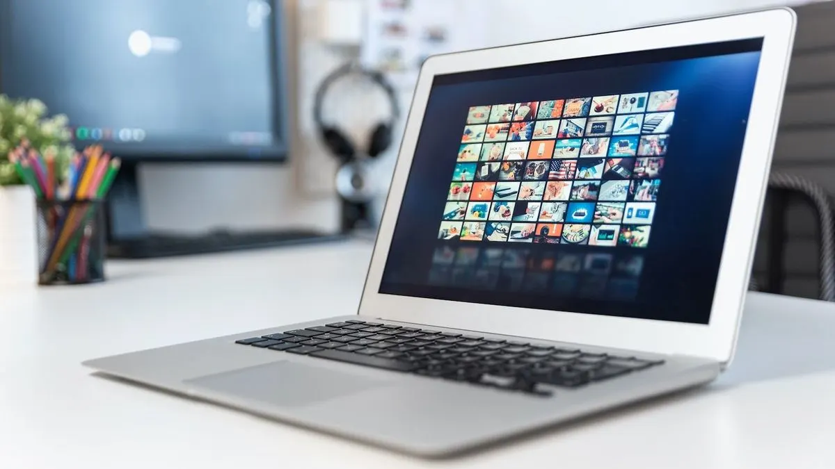 Laptop mit vielen Bild-Icons auf dem Bildschirm steht auf Schreibtisch.