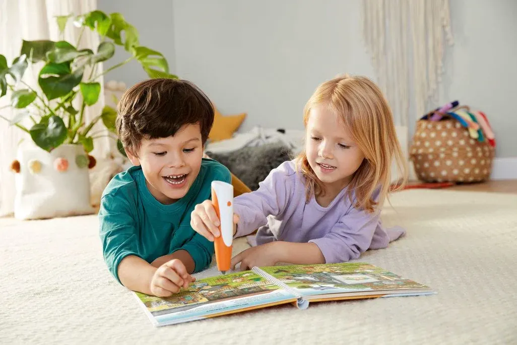 2 Kinder liegen am Boden und spielen mit Tiptoi