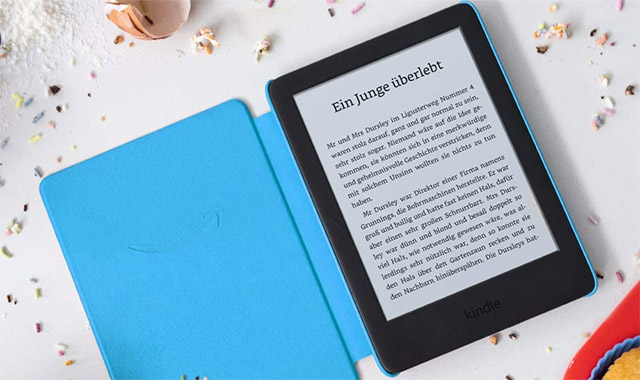 Ein E-Reader mit blauem Cover zeigt Text auf einem hellen Bildschirm. Streusel und eine Schüssel liegen im Hintergrund.