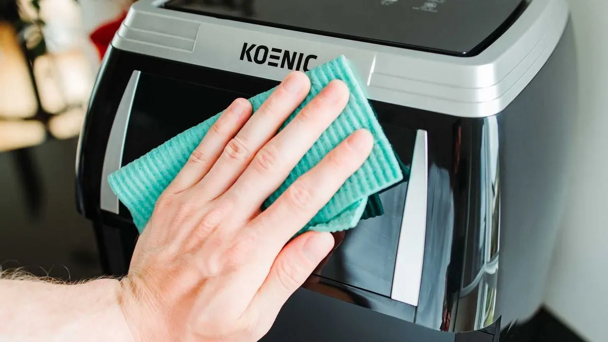 Hand wischt mit einem Tuch ueber Oberflaeche einer Koenic Heissluftfritteuse