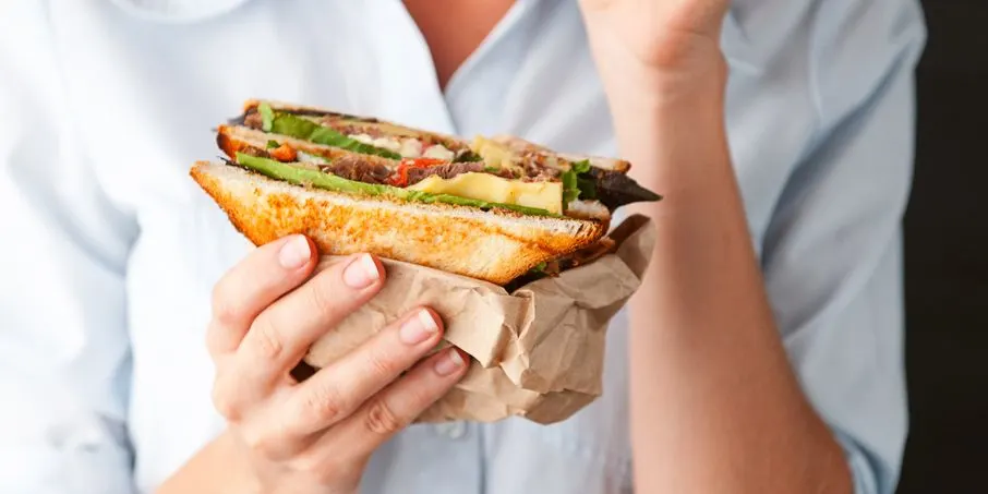 Person hält Sandwich mit Salat Käse und Tomate in der Hand
