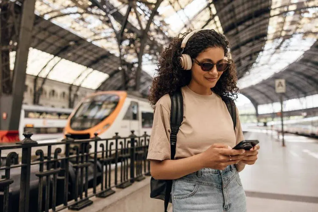 Frau mit Kopfhörern schlägt am Bahnhof etwas auf einem Smartphone nach.