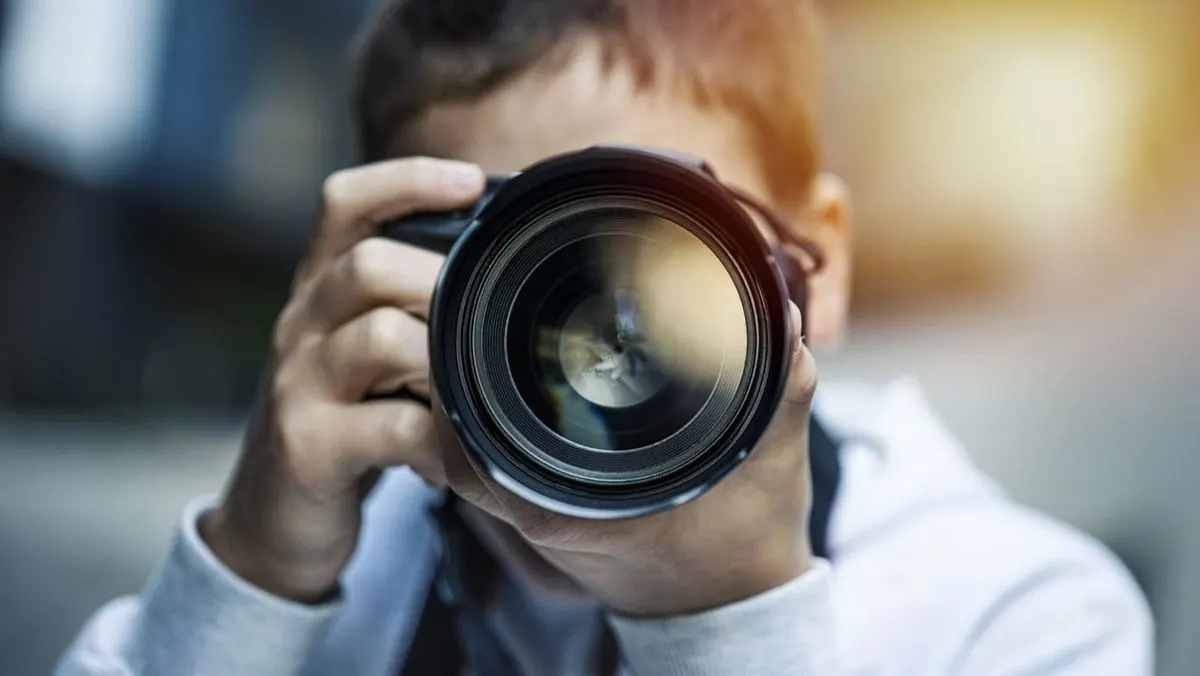 Mann hält eine große Spiegelreflexkamera und fotografiert.