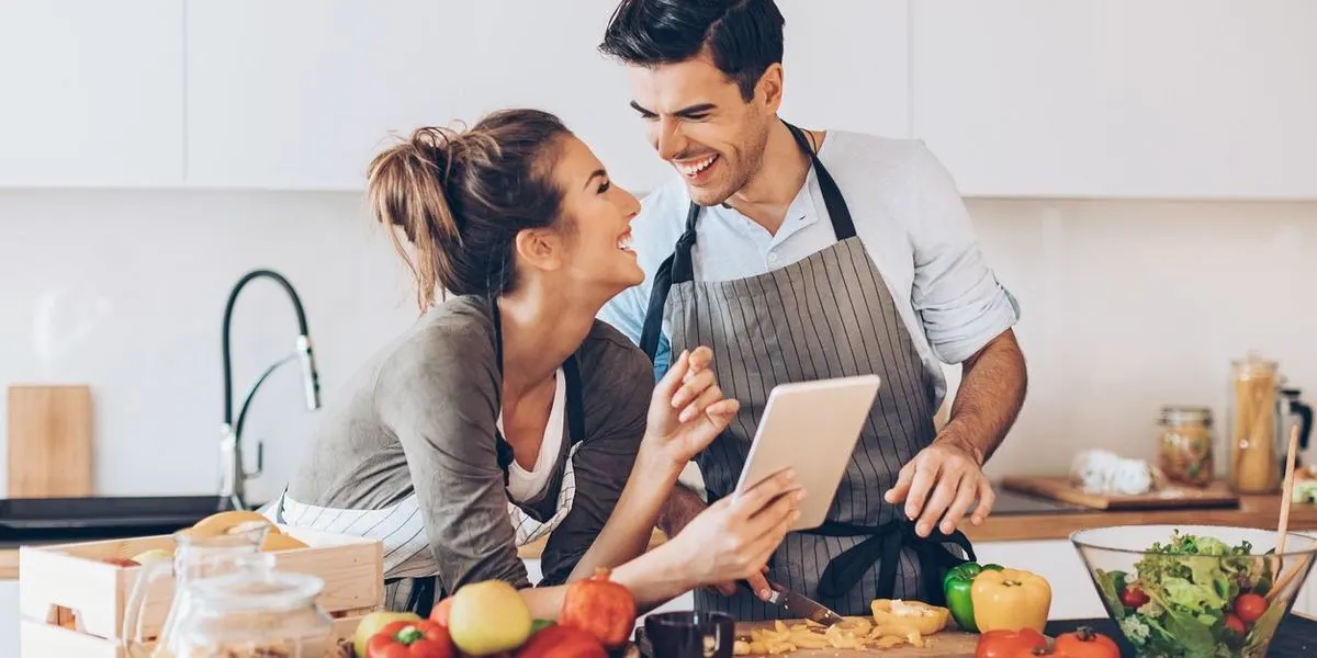 Zwei Personen bereiten eine Mahlzeit in einer Küche zu und schauen auf ein Tablet.