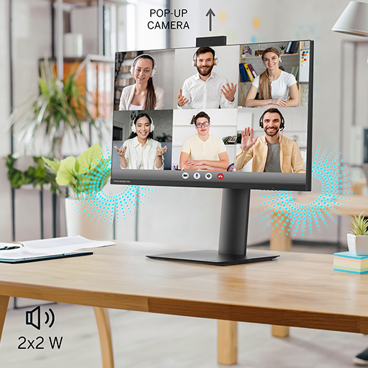 Ein schwarzer Monitor zeigt ein Videokonferenzgespräch auf einem Holztisch mit Pflanzen im Hintergrund.