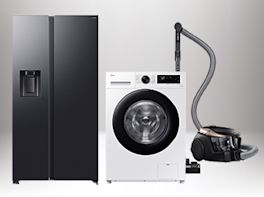 Drei Haushaltsgeräte — ein schwarzer Side-by-Side-Kühlschrank mit Wasserspender, eine weiße Frontlader-Waschmaschine und ein schwarzer Bodenstaubsauger mit Schlauch.