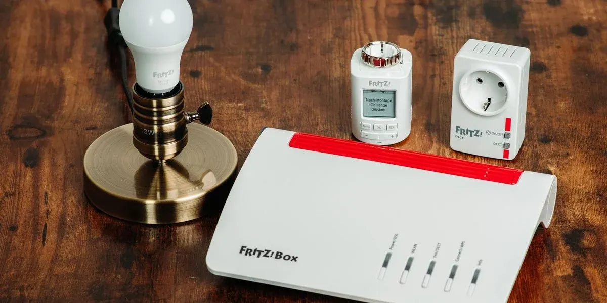 Fritz!Box Router, LED-Lampe in Bronzesockel, weißer Thermostat mit Display und smarter Zwischenstecker auf Holz.
