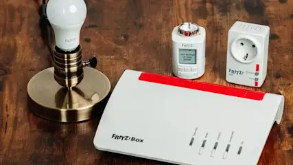 Fritz!Box Router, LED-Lampe in Bronzesockel, weißer Thermostat mit Display und smarter Zwischenstecker auf Holz.