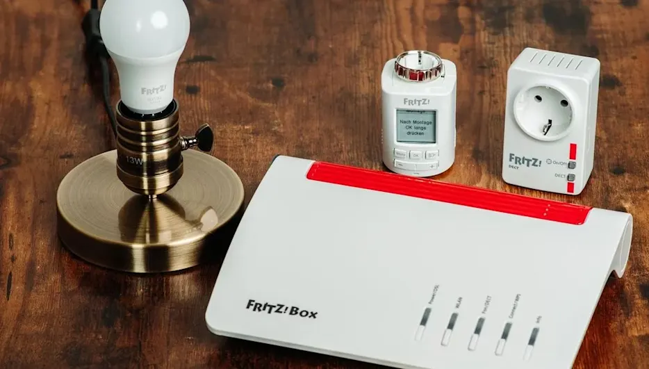 Fritz!Box Router, LED-Lampe in Bronzesockel, weißer Thermostat mit Display und smarter Zwischenstecker auf Holz.