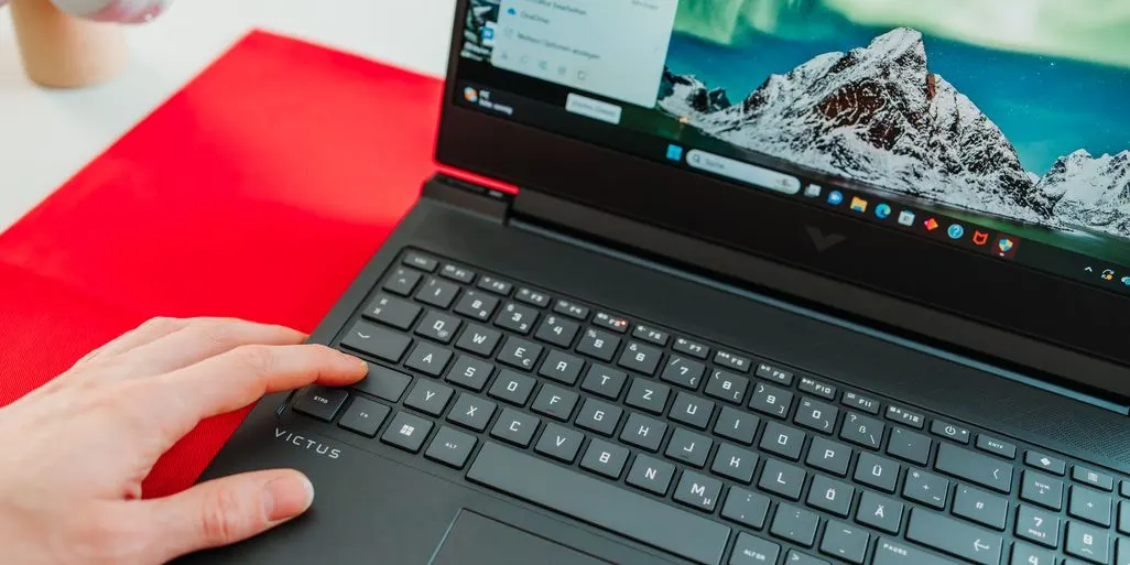 Hand tippt auf Victus Gaming-Laptop mit Berglandschaft-Hintergrund auf Bildschirm