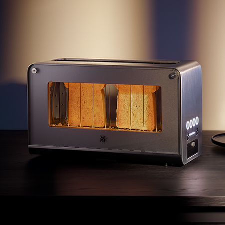 Ein grauer Toaster mit Sichtfenster steht auf einem dunklen Tisch. Im Inneren sind zwei Toastscheiben sichtbar.