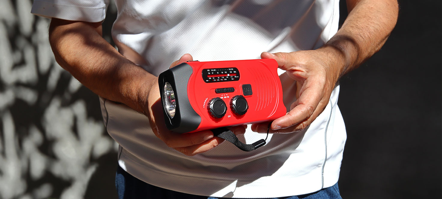 Eine rote Notfallkurbelradio mit schwarzem Akzenten wird vor einem weißen T-Shirt gehalten.