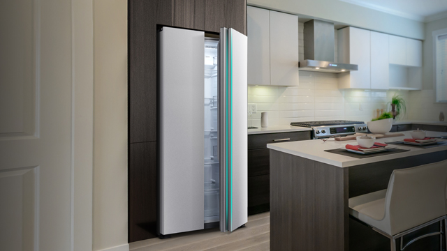 Ein Kühlschrank mit zwei Türen steht leicht geöffnet in einer Küche mit grauen und weißen Schränken und einer Kochinsel.