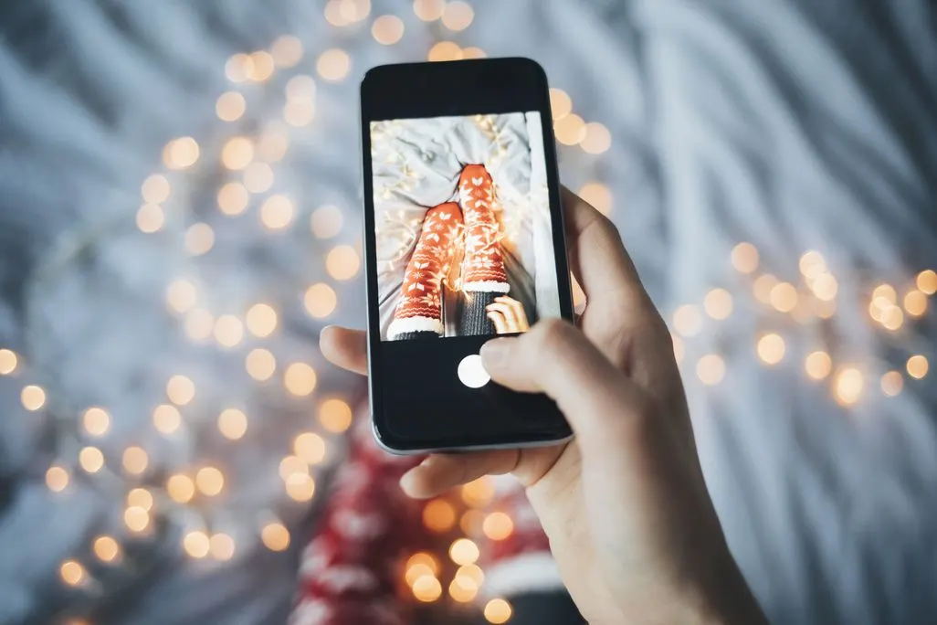 Eine Person fotografiert ihre Beine in roten Weihnachtssocken mit einem Smartphone.