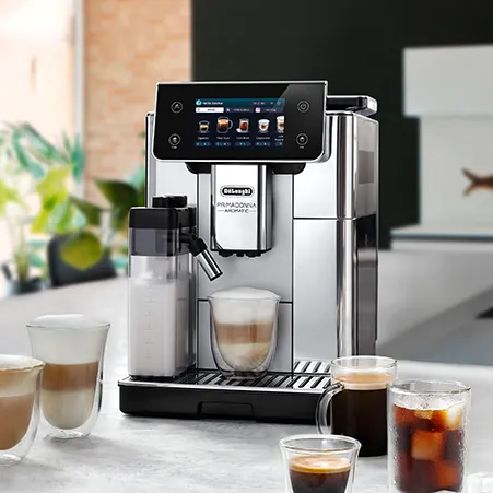 Silberne Kaffeemaschine mit Milchbehälter und verschiedenen Getränken auf einem Tisch. Mehrere Gläser mit Kaffee sind zu sehen.