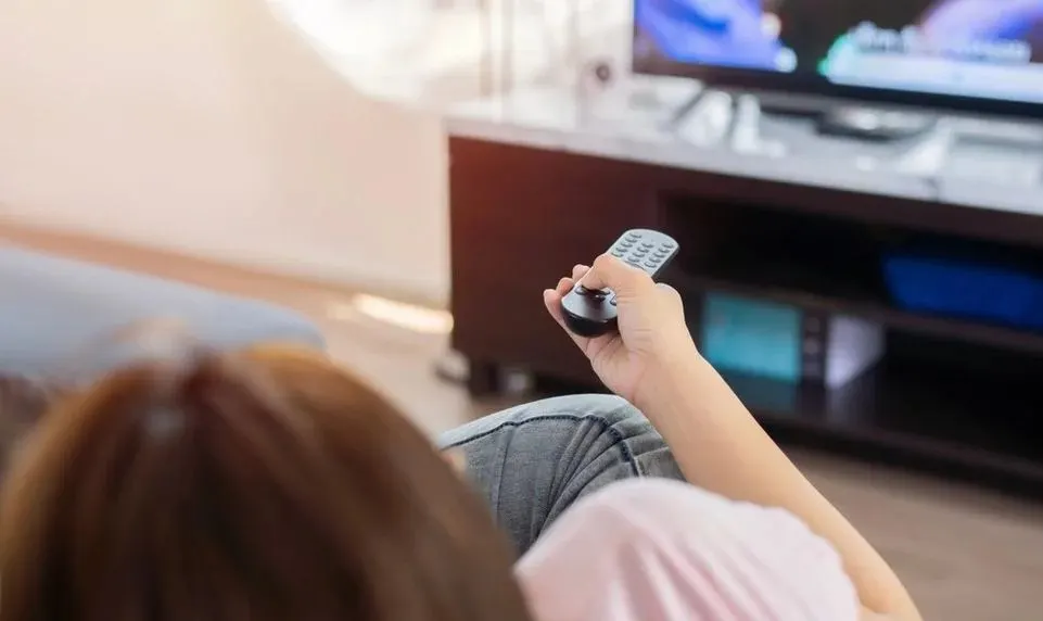 Person sieht fern und bedient den Fernseher mit Fernbedienung