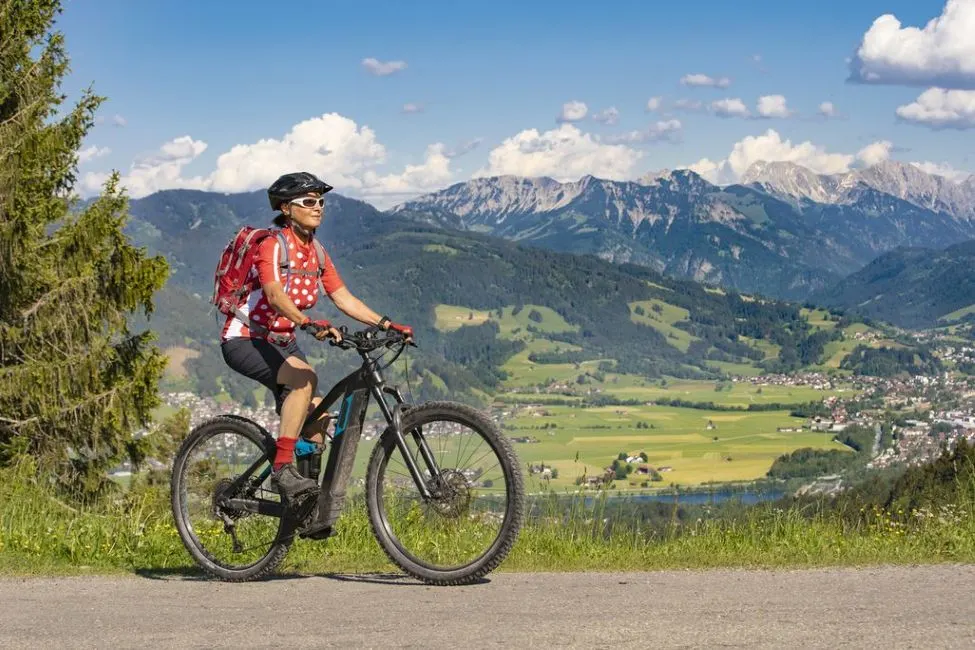 Radfahrer mit rotem Rucksack faehrt auf einem E Bike vor Berglandschaft