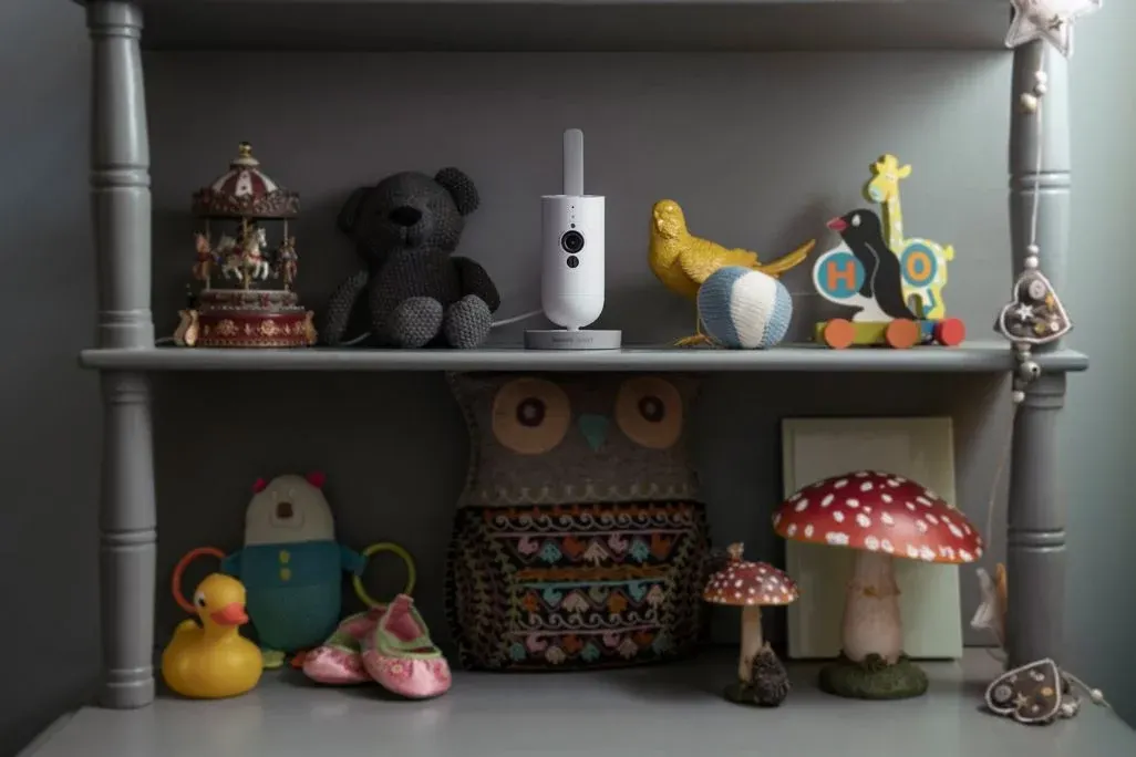 Babyzimmer-Regal mit verschiedenen Spielzeugen und Dekofiguren, in deren Mitte eine weiße Babycam mit Antenne steht.