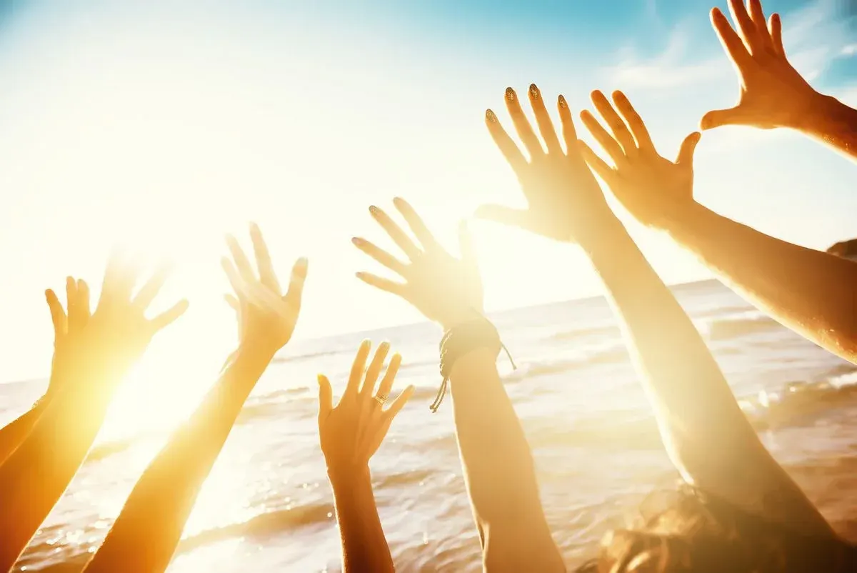 7 Hände die sich am Strand gegen den Himmel strecken mit Sonne
