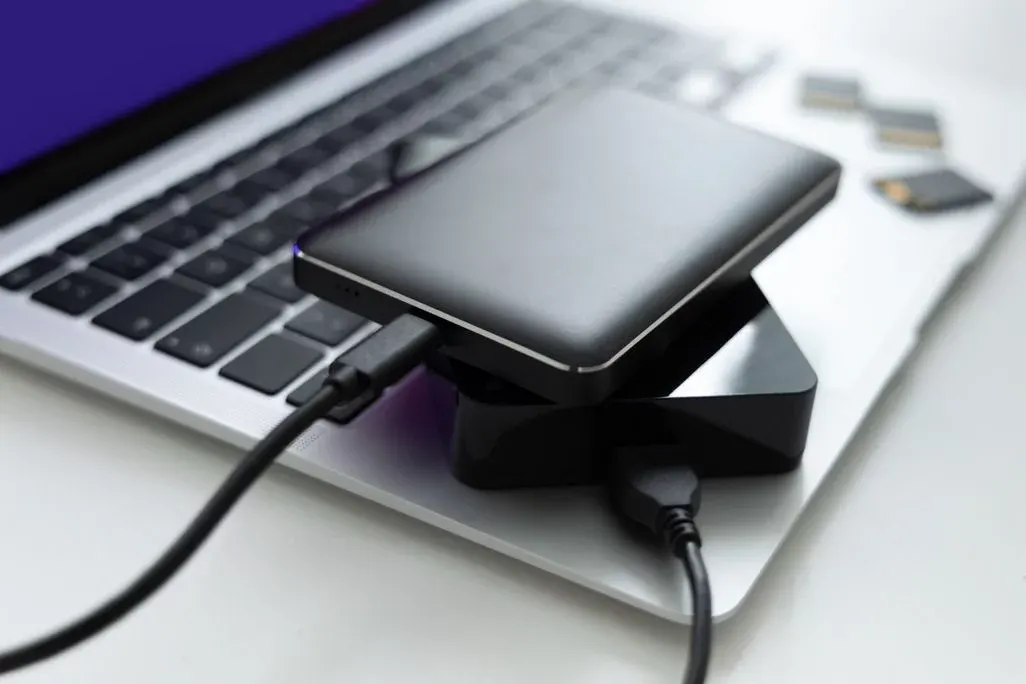 Smartphone lädt an Laptop via USB-Kabel mit Ladeadapter neben Tastatur.