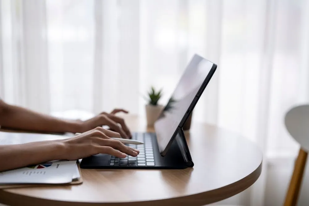 Frau nutzt Tablet mit externer Tastatur an einem runden Schreibtisch.
