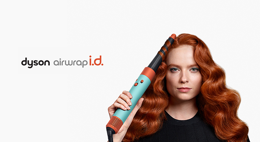 Ein Dyson Airwrap Haarstyler mit blaugrünem Griff und orangefarbenen Akzenten wird vor einem weißen Hintergrund präsentiert.