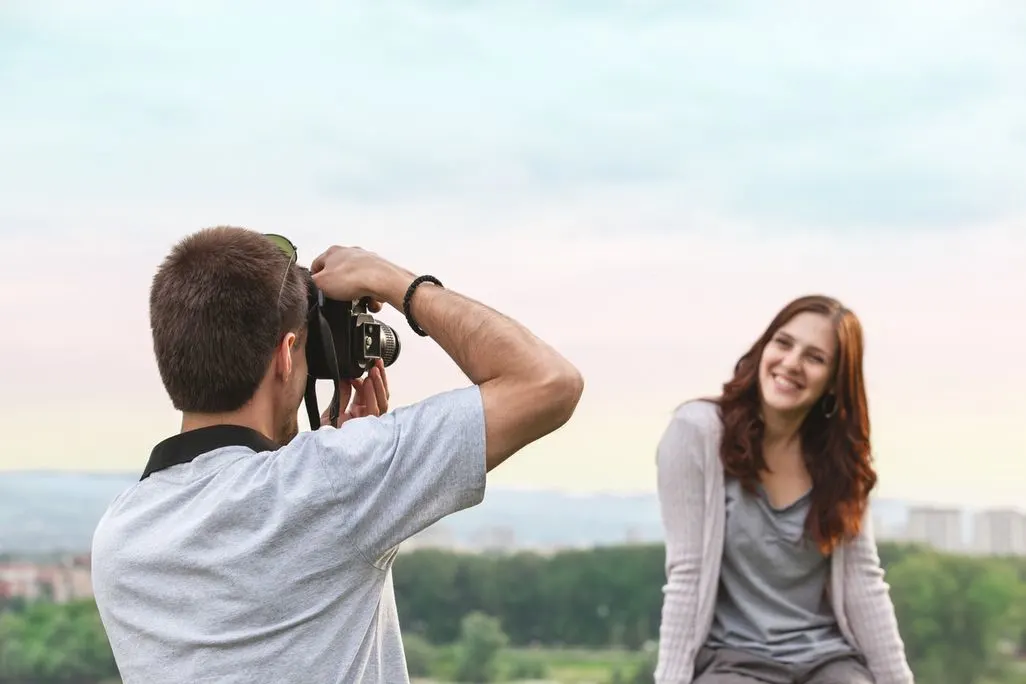 Mann fotografiert eine Frau im Freien vor einer Landschaft