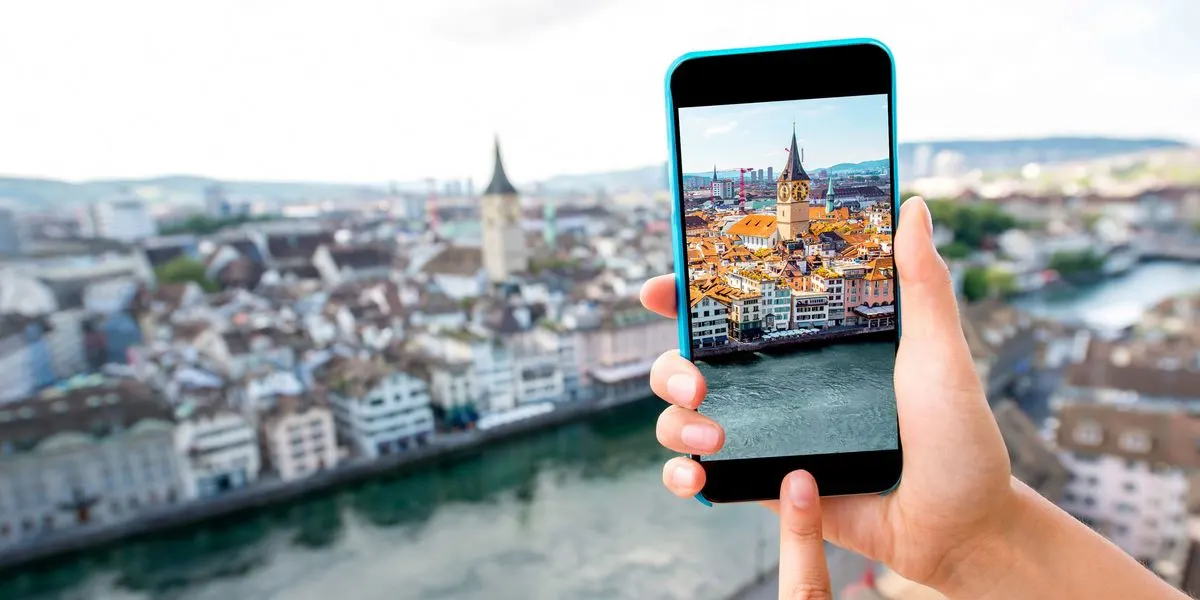 2 Hände, die mit einem Smartphone ein Foto von einer Stadtansicht mit Fluss und Kirchturm machen.