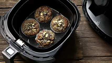 Vier Muffins mit Kernen in einer Heißluft Fritteuse auf einem Holzuntergrund.