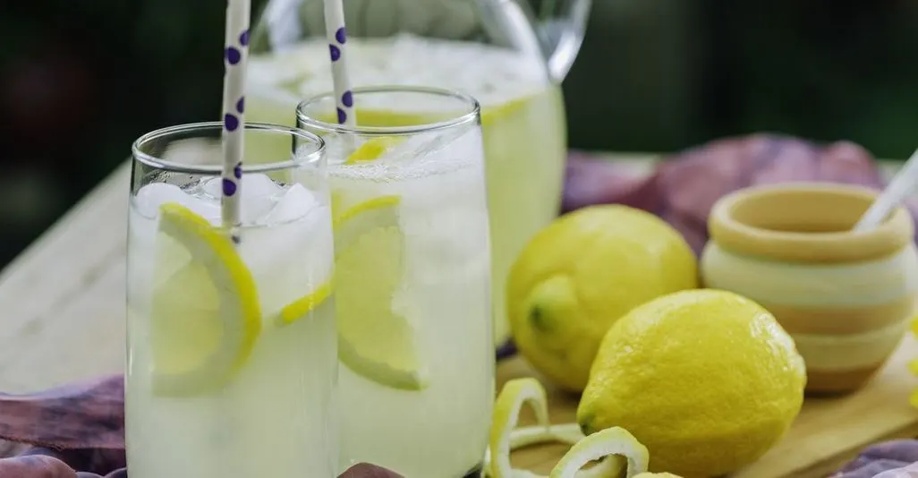 Gläser mit Limonade, Zitronenscheiben und Eiswürfeln neben ganzen Zitronen.