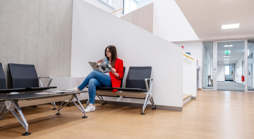 Frau sitzt auf einem Sessel im Wartebereich und blättert in einer Zeitung